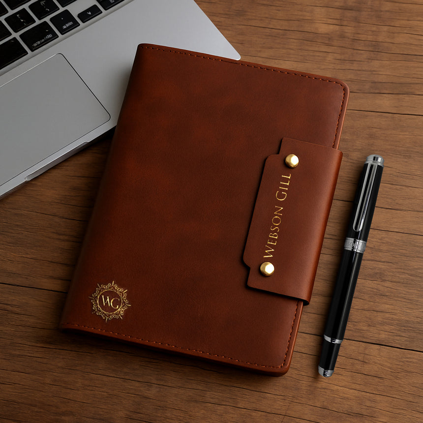 Webson Gill Leather Writing Notebook, embossed with the brand name, sits beside a pen and laptop on a wooden desk—a perfect fountain pen notebook for capturing your thoughts.