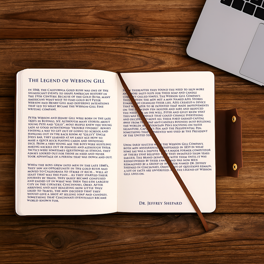 A Webson Gill Leather Writing Notebook lies open on a wooden desk beside a wand and laptop, displaying a story titled "The Legend of Webson Gill.