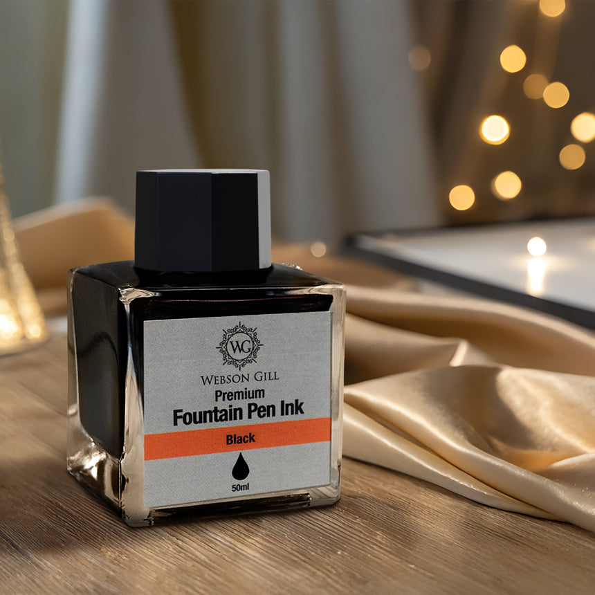 A bottle of Webson Gill's 'Ink in a Bottle' Fountain Pen Refill—black ink that fits all fountain pens—rests on a wooden surface with golden fabric and softly blurred lights in the background.