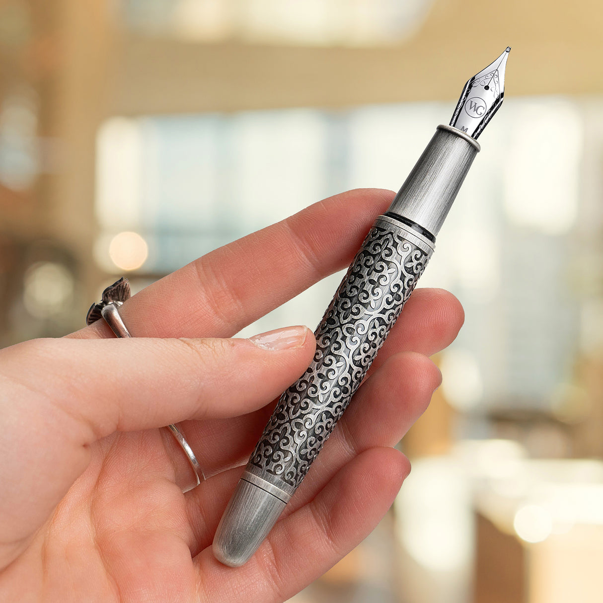 A hand holds the 'Admiral' Premium Fountain Pen by Webson Gill, featuring intricate silver swirling patterns—an ideal choice for a luxury gift.
