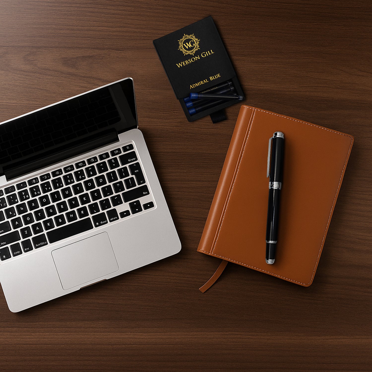 A laptop, a brown notebook, and The Mogul Fountain Pen by Webson Gill with blue ink cartridges are arranged on a wooden desk.