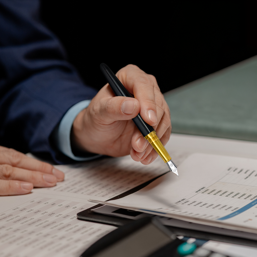 A person reviews financial documents with a Webson Gill 'Captain Edition' Premium Fountain Pen in Black Wood, featuring a stainless steel nib, alongside papers and a calculator on the desk.