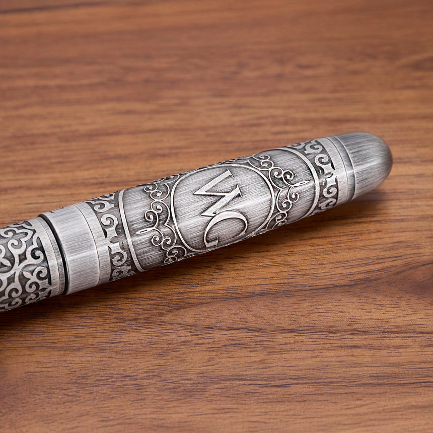 The 'Admiral' Premium Fountain Pen by Webson Gill, featuring ornate engravings and "WC" initials, rests on a wooden surface—an antique-style luxury silver fountain pen crafted for elegance.