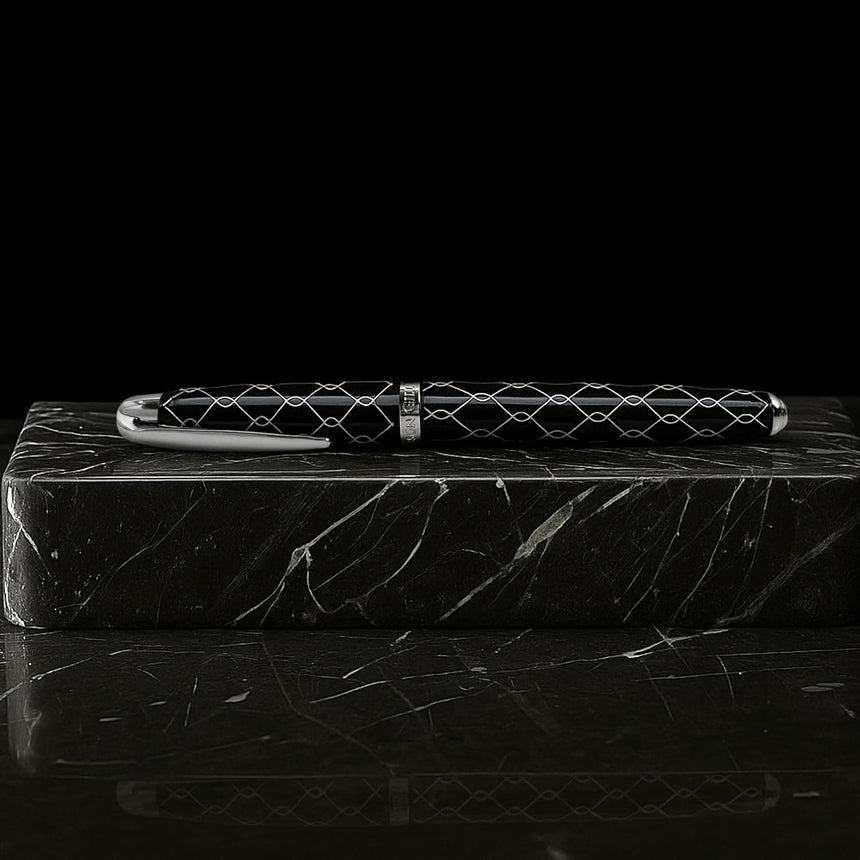 The WG ‘The Weaver’ Everyday Fountain Pen features a silver lattice design and a stainless steel medium nib, resting on a black marble block and promising smooth writing against a dark background.