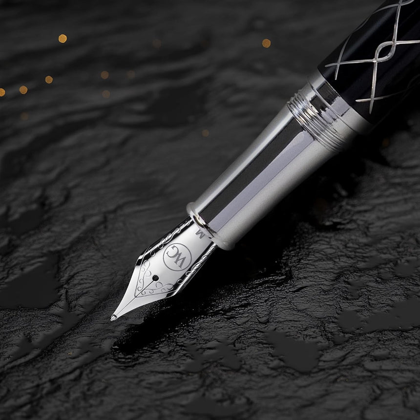 Close-up of WG’s ‘The Weaver’ Everyday Fountain Pen, featuring a silver lattice design and stainless steel medium nib, resting on a textured black surface with golden highlights for a smooth writing experience.
