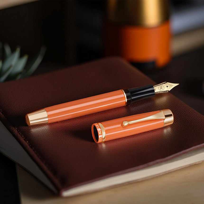 The Muse Fountain Pen by Webson Gill, featuring a gold-plated nib, rests with its cap on a closed brown leather notebook—melding elegance and ergonomic design.