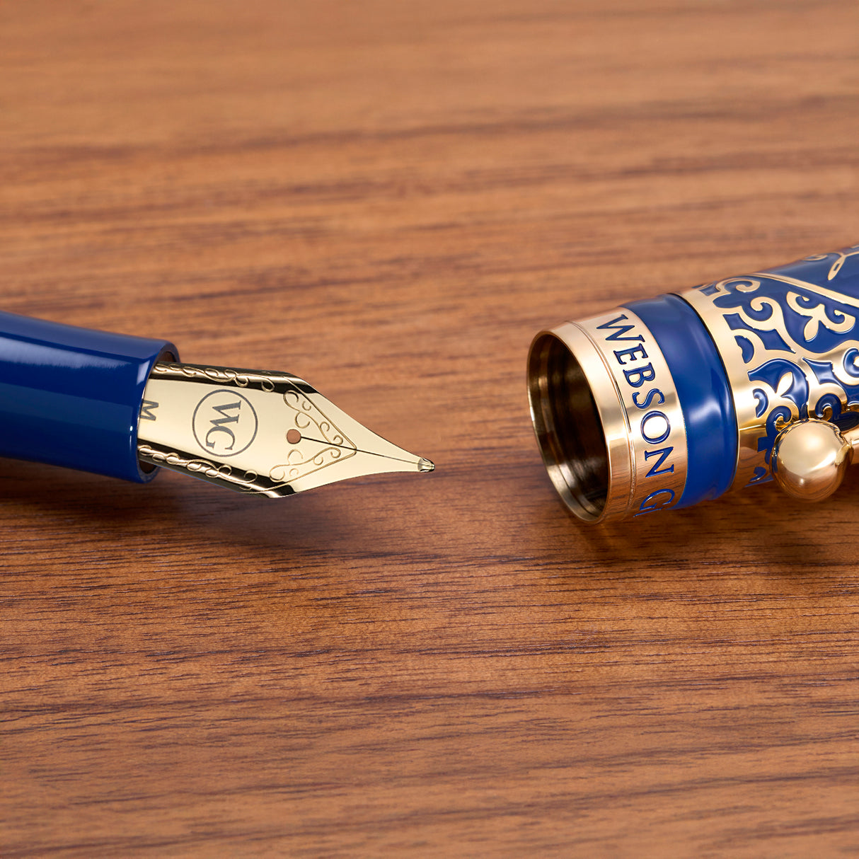 Close-up of Webson Gill’s 'The Regal' Premium Fountain Pen with blue and gold brass filigree, uncapped on a wooden surface—a collector's dream for fountain pen enthusiasts.