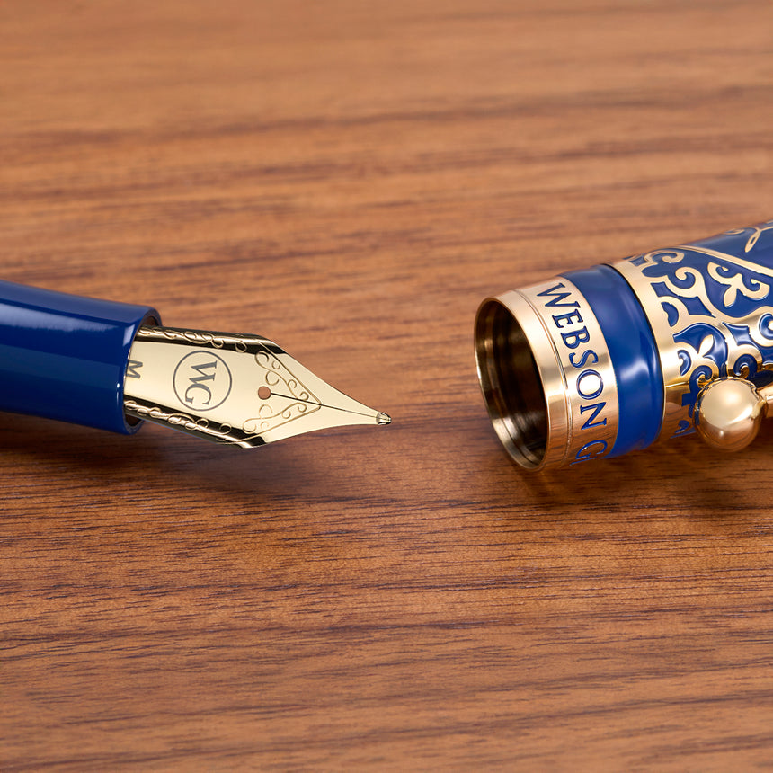 Close-up of Webson Gill’s 'The Regal' Premium Fountain Pen with blue and gold brass filigree, uncapped on a wooden surface—a collector's dream for fountain pen enthusiasts.