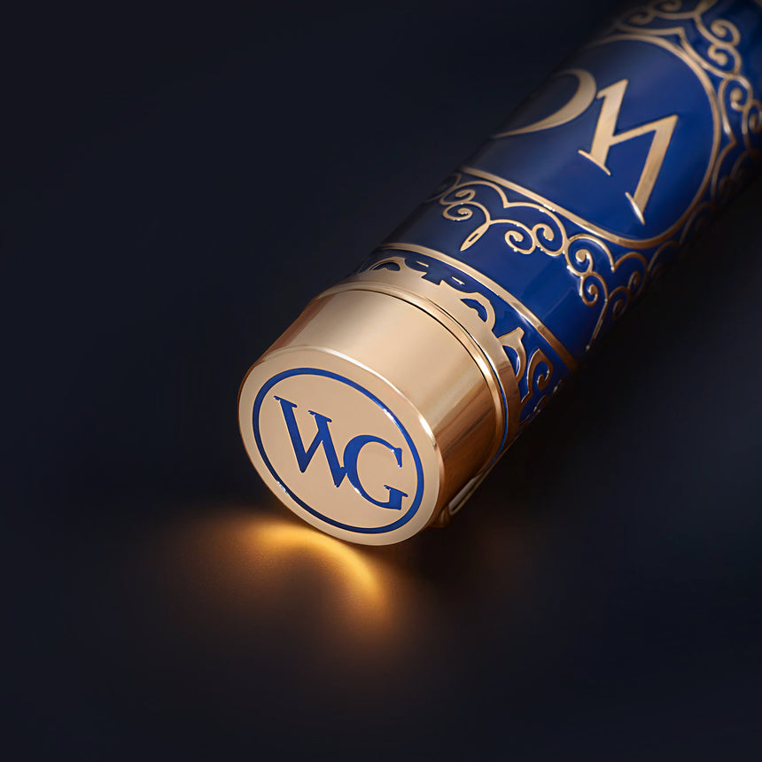 A blue and gold tube with ornate patterns and brass filigree, its cap labeled "WG" and glowing softly—The Regal Premium Fountain Pen from Webson Gill is a true treasure for collectors.