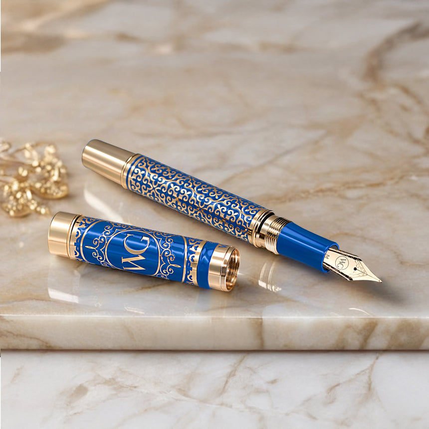 The Regal Premium Fountain Pen by Webson Gill features intricate gold brass filigree on a blue and gold designer cap, elegantly displayed on polished marble—an exquisite choice for discerning fountain pen collectors.