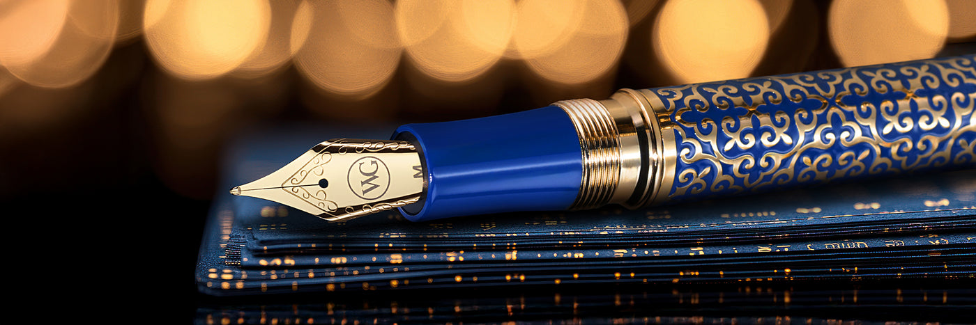 A decorative fountain pen with a gold nib rests on patterned blue notebooks against a blurred golden background.