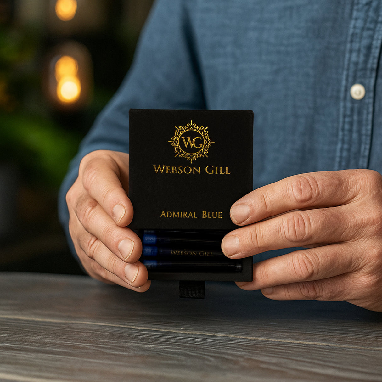 A person holds a Webson Gill Blue Ink Refill Starter Pack box with gold lettering on a wooden table.