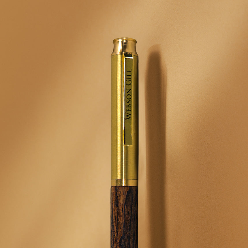 Close-up of the Webson Gill Prestige Edition Fountain Pen, featuring a gold and wood design with "WEBSON GILL" engraved on the clip and an iridium nib, set against a beige background.