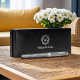 The Webson Gill Admiral Fountain Pen, featuring an antique silver finish, rests in a black branded box on a table, highlighting its elegant design and craftsmanship with white flowers in the background.