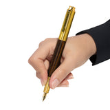 A hand holds the Webson Gill Prestige Edition Fountain Pen, featuring a gold and wood finish with an iridium nib, ready to write against a white background.