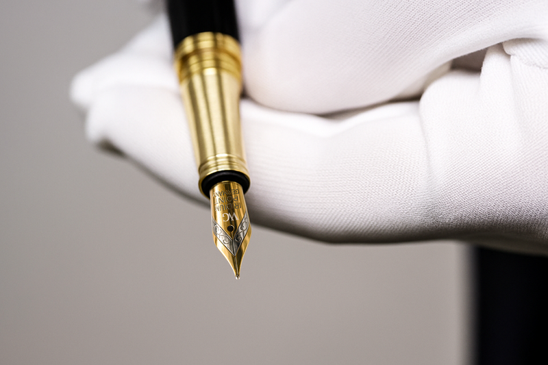 A gloved hand holding a gold and black fountain pen with an ornate nib.