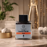 A jar of Webson Gill Black Ink, a universal fountain pen refill by Webson Gill, rests on a marble table—an ideal choice for calligraphy lovers, surrounded by plants and chic decor.