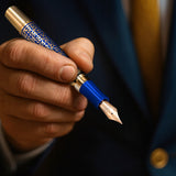A person in a suit holds The Regal Fountain Pen by Webson Gill, featuring blue enamel and gold brass filigree—an ideal choice for collectors who appreciate ornate design.