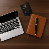 A laptop, a brown notebook, and The Mogul Fountain Pen by Webson Gill with blue ink cartridges are arranged on a wooden desk.
