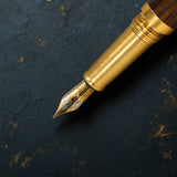 A close-up of the Webson Gill Prestige Edition Fountain Pen, featuring a gold iridium nib, resting on a textured black surface.