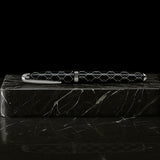 The WG ‘The Weaver’ Everyday Fountain Pen features a silver lattice design and a stainless steel medium nib, resting on a black marble block and promising smooth writing against a dark background.