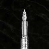 The WG ‘The Mirror’ Everyday Fountain Pen, featuring a silver metal body with a patterned barrel and stainless steel nib, rests elegantly on a black marble background.