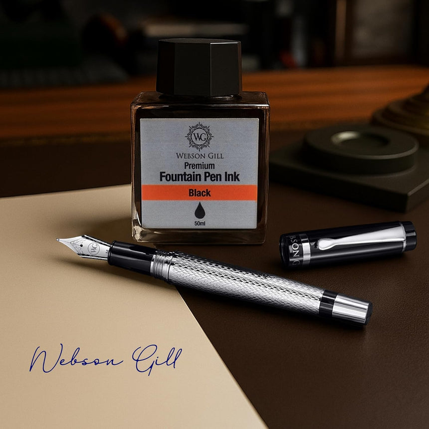 ‘The Raider’ Everyday Fountain Pen by WG, featuring a stainless steel medium nib, rests next to a black WG ink bottle on a desk with paper and the pen cap.
