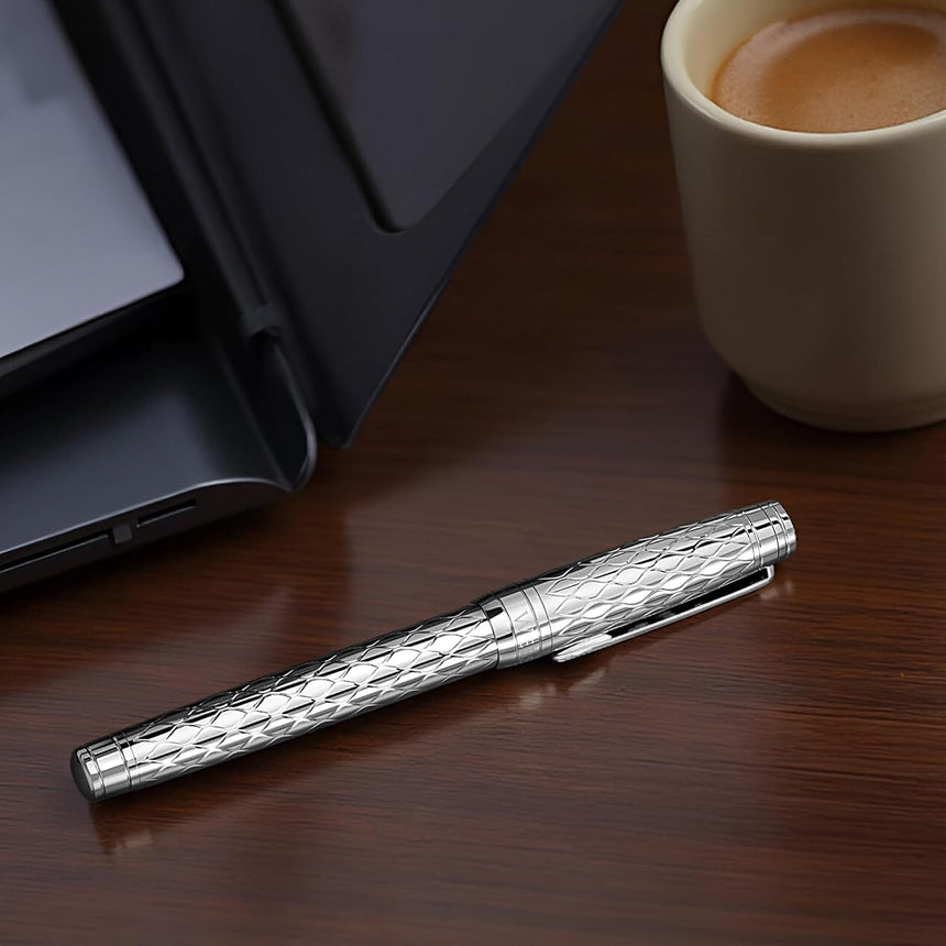 WG’s ‘The Mirror’ Everyday Fountain Pen, featuring a stainless steel nib, rests on a wooden desk next to a laptop and a cup of coffee.