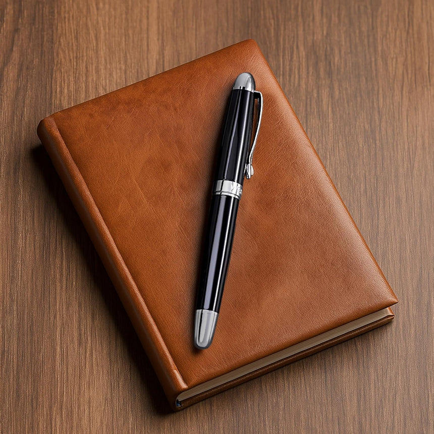 The WG 'The Boss' Everyday Fountain Pen, featuring a stainless steel nib and black finish, rests atop a closed brown leather notebook on a wooden surface.