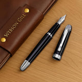 A black 'The Boss' Everyday Fountain Pen by WG, featuring a stainless steel nib and silver accents, rests in a brown leather case marked "WEBSON GILL" on a wooden surface.