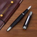 The WG 'Show Up' Everyday Fountain Pen in black and silver with a stainless steel medium nib rests uncapped next to a brown leather notebook on a wooden desk.