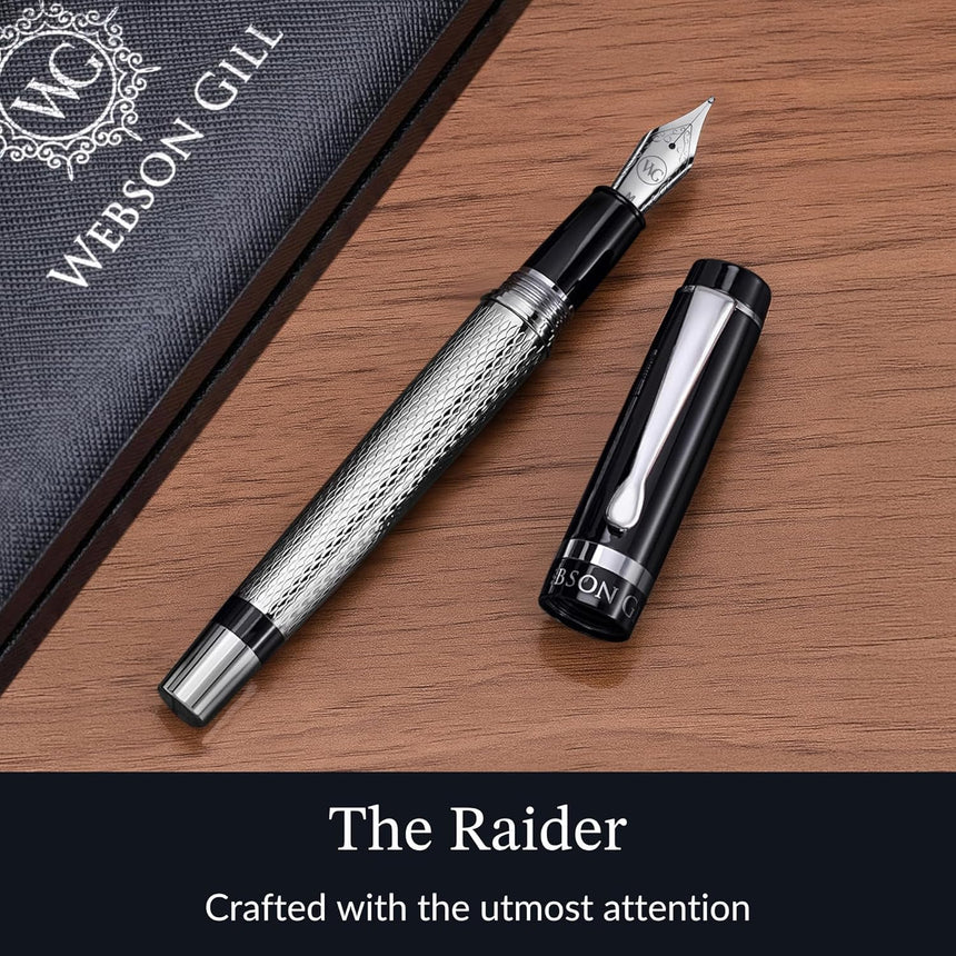 A black and silver WG ‘The Raider’ Everyday Fountain Pen with its cap off and a stainless steel medium nib rests on a textured surface beside a Webson Gill box.