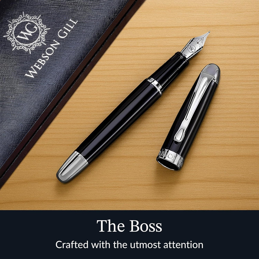 The WG 'The Boss' Everyday Fountain Pen, featuring a black and silver design with a stainless steel nib, rests on a wooden surface beside its case.