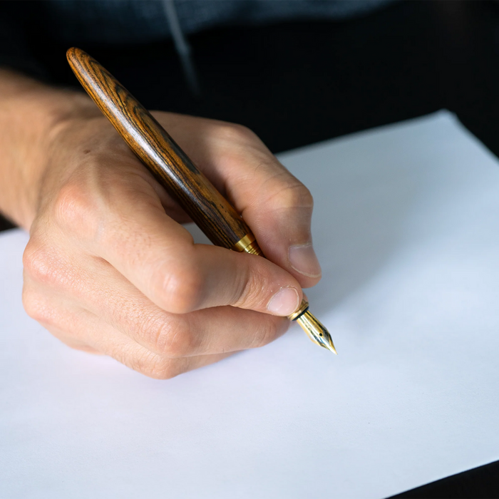 A hand holds the Webson Gill Captain Edition Fountain Pen, featuring a wooden barrel and stainless steel nib, poised over a blank white sheet ready to write.