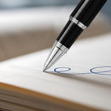 A close-up of 'The Mogul' Premium Ballpoint Pen by Webson Gill, featuring a smooth ink flow as it writes a blue ink signature on white paper.
