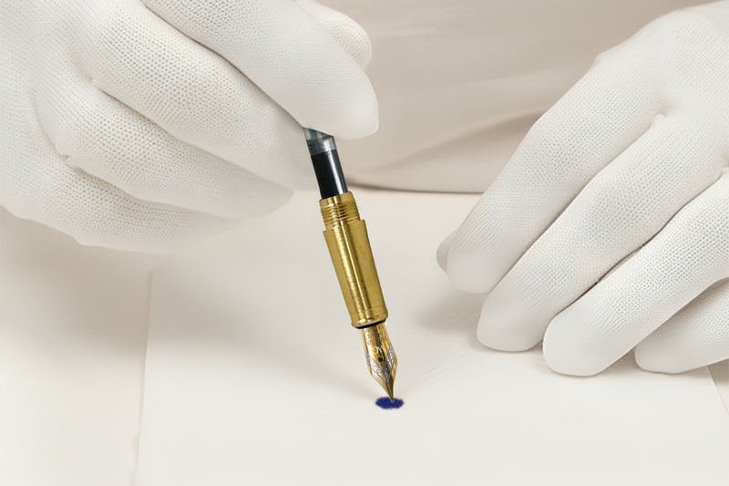 Gloved hands holding a fountain pen, making a small ink mark on white paper.