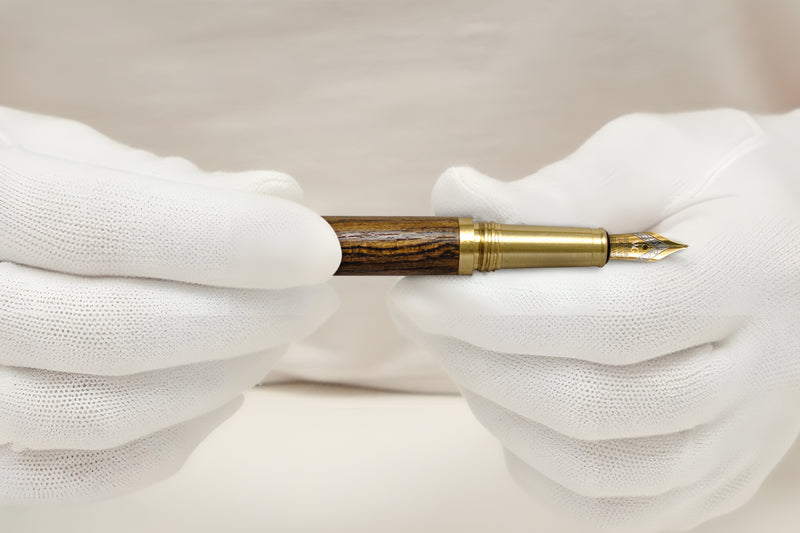 Gloved hands holding a vintage fountain pen with a wooden barrel and gold nib.