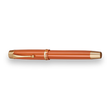The Muse Fountain Pen by Webson Gill, with an orange body, gold-plated nib, gold accents, and a clip, is displayed on a white background.