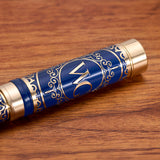 The Regal Fountain Pen by Webson Gill features blue and gold accents with ornate brass filigree and "WC" lettering. This luxury pen rests elegantly on wood, making it perfect for collectors.