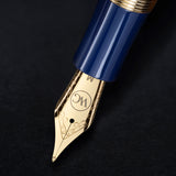 Close-up of The Regal Fountain Pen nib by Webson Gill, featuring ornate gold brass filigree and a blue pen body on a black surface—ideal for fountain pen collectors.