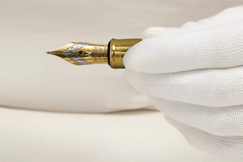 A gloved hand holding a gold-tipped fountain pen against a white background.